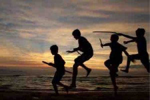 Four children with sticks in silhouette, jumping on a Lake Michigan beach after sunset