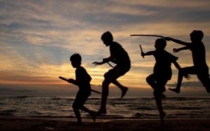 Children in silhouette play on a beach at dusk