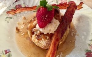 Closeup of a pretty dish with French toast garnished with whipped cream, strawberry and two strips of bacon