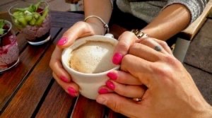 Unseen man holds the hand of an unseen woman who is cradling a coffee cup.