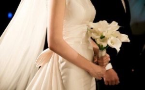 The torso of a bride in a creamy dress carrying a bouquet