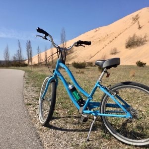 Blue bike stands along paved trail with Sleeping Bear Dunes in background.