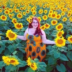 Model and fashion blogger Briana Herzog poses in a vintage-style floral dress in a field of sunflowers.