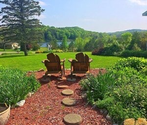Two Adirondack chairs whose backs are carved in the shape of Michigan’s Lower Peninsula sit on the front yard at House on the Hill B&B, offering views of an expansive lawn and a lake.