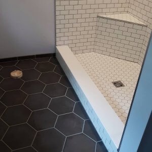Dark six-sided tiles of a bathroom contrast with creamy white tiles in the shower.