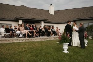 Guests sit on a patio as bride, groom, and officiant speak the words.