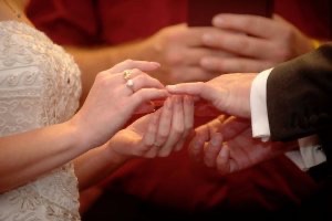 Closeup photo of bride placing a ring on the groom’s finger.