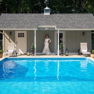 A bride stands in the shade of a building o the property of Villa on Verona while the foreground is filled with th bright blue of the swimming pool.