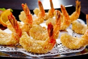 Toasted coconut coats shrimp with tails on standing on a serving dish.