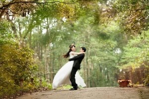 Just-married couple embrace on a dirt road under tall trees