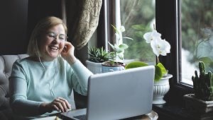Smiling woman engages on her laptop with someone unseen on the screen.