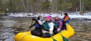 Women help paddle a guided raft on the Jordan River in a Michigan winter getaway