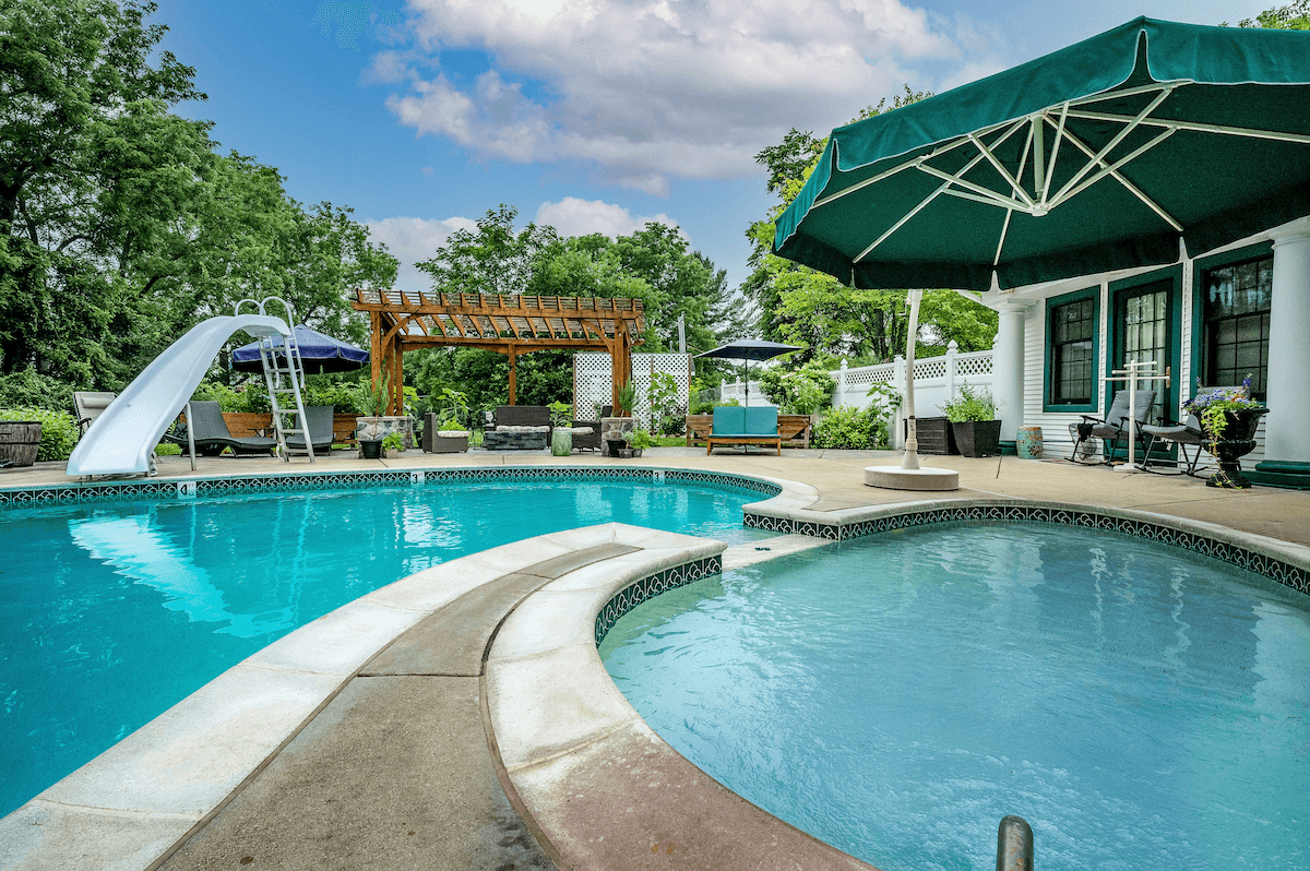 Outdoor pool with green umbrella and veranda at the Maple Cove Boutique Bed and Breakfast