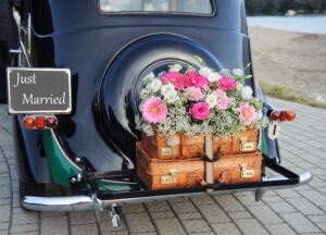 Bridal bouquet and suitcases tied to the trunk of an old car