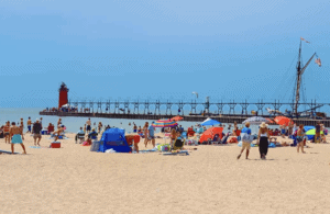 South Haven Beach in Michigan with numerous sunbathers and umbrellas. A lighthouse with a board walk is in the background