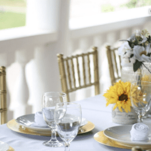 Beautiful Table with white tablecloth gold chairs, table setting and a flower bouquet with yellow flowers