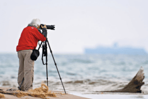 Man in a red jacket taking a picture on a beach