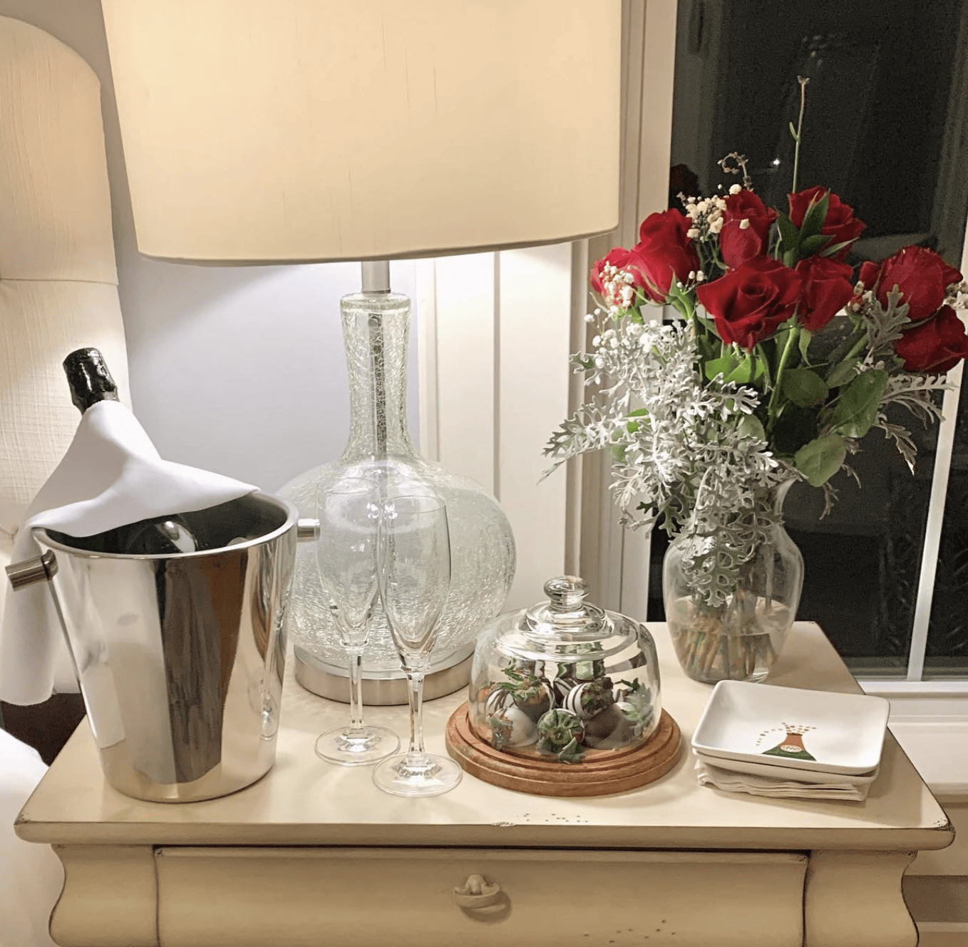 Side table that includes a bottle of bubbly, roses and chocolate