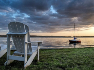 Adirondack Chair beside a lake at sunset with distant views of a moored sailboat
