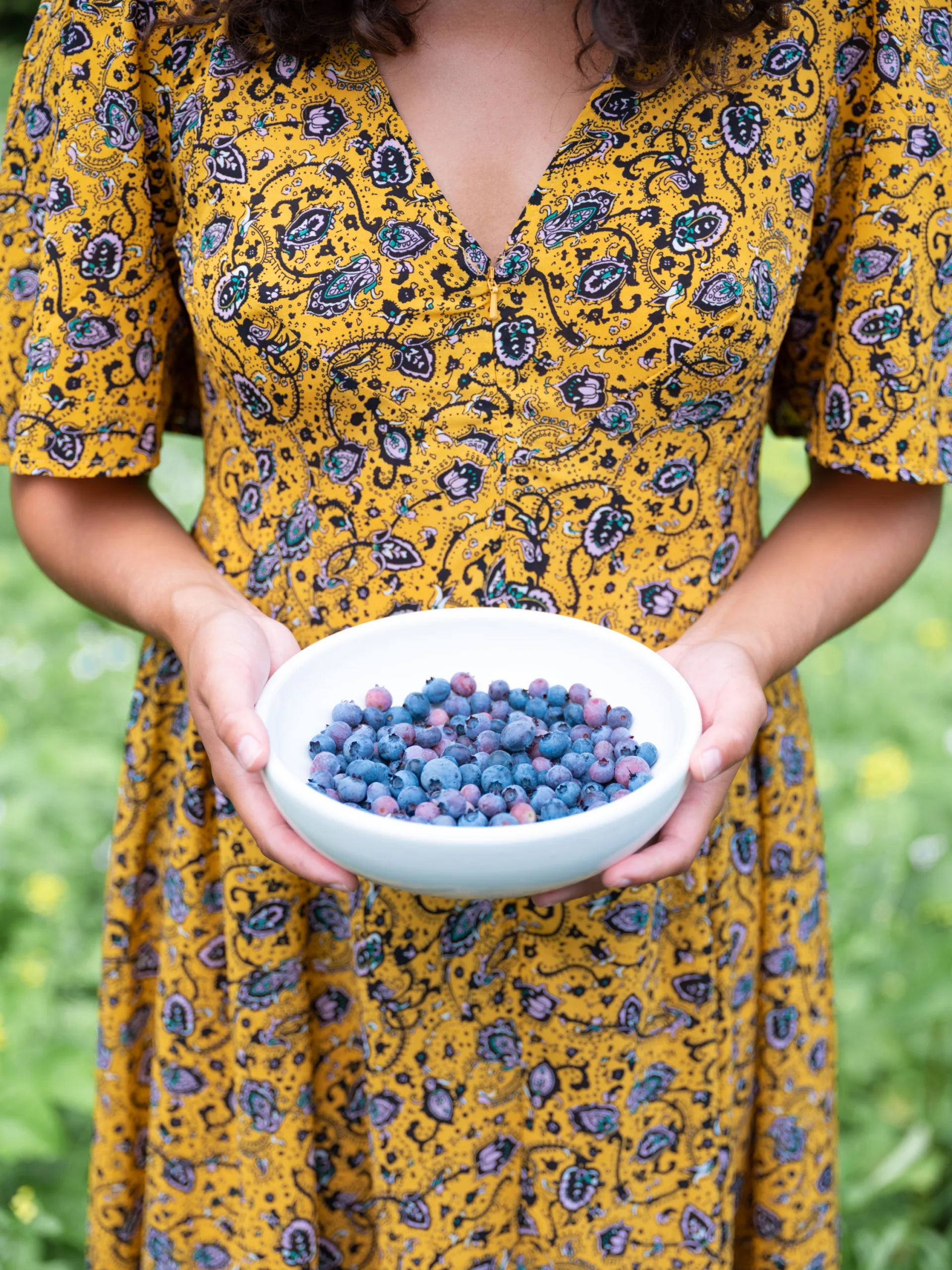 Woman in a yellow and blue dress holding a bowl full of Blueberries