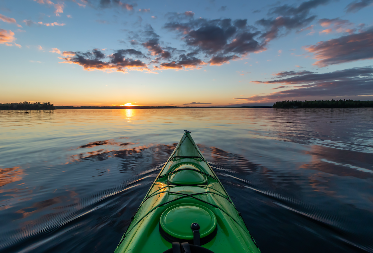 Green kayak moving across water during sunrise
